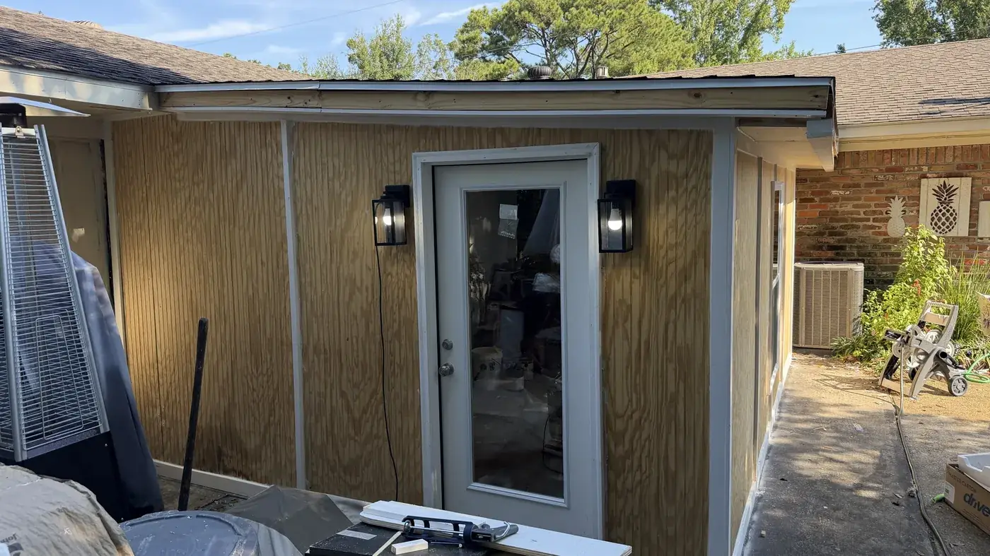 Carport enclosure framed, sheathed and trimmed with a new exterior door, wall sconces and roofline tied into the existing brick house