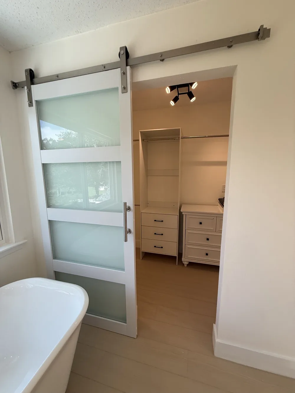 Frosted glass barn door slid open to a walk-in closet with new shelving and track lighting