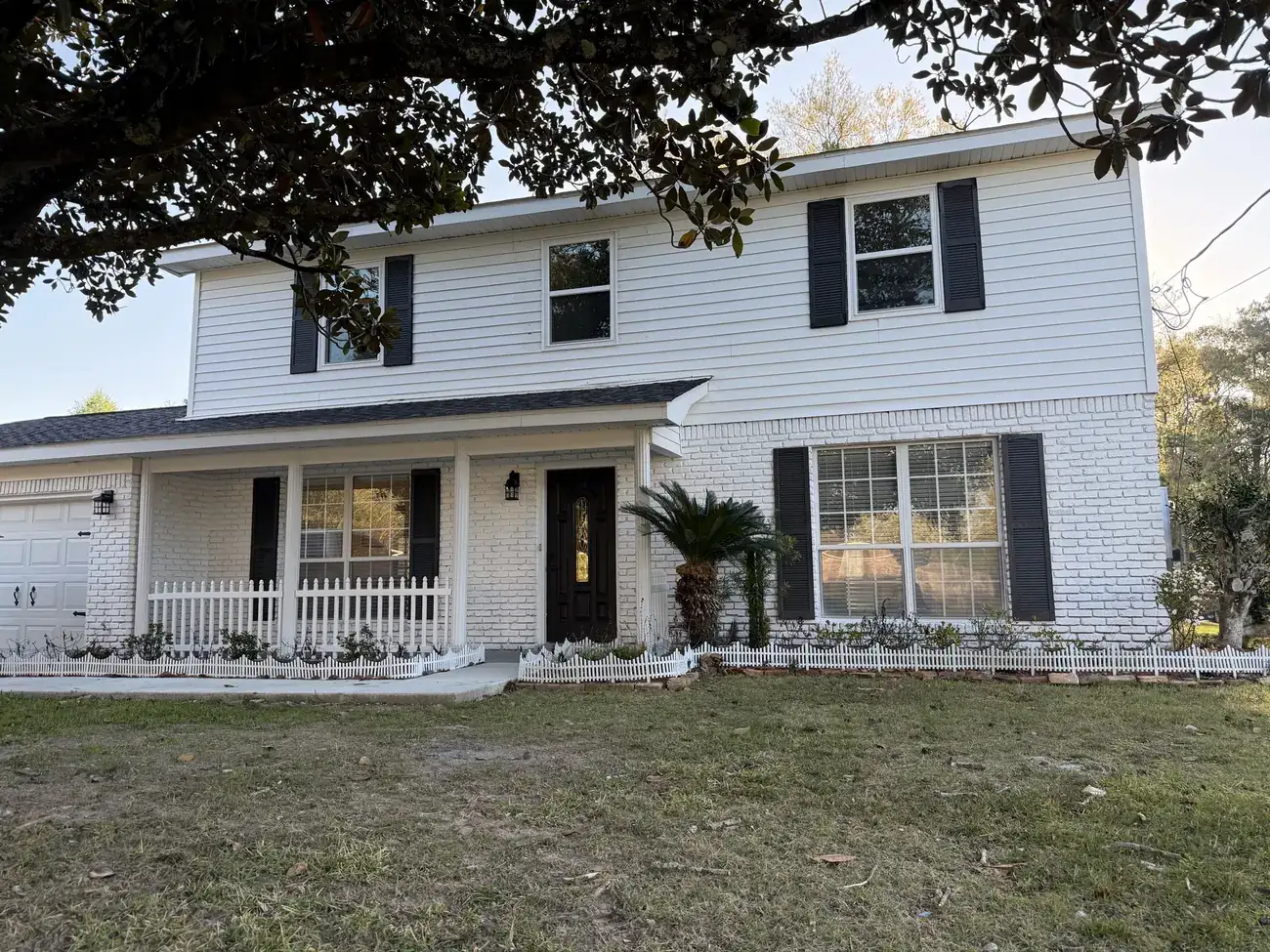 Front elevation of the finished two-story flip showing new roof, painted brick, black shutters and picket-fence flower beds