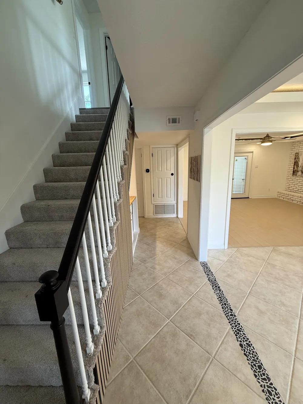 Entry foyer with carpeted stairs, black handrail, white spindles, a wood-slat accent wall and tile with a pebble mosaic inlay