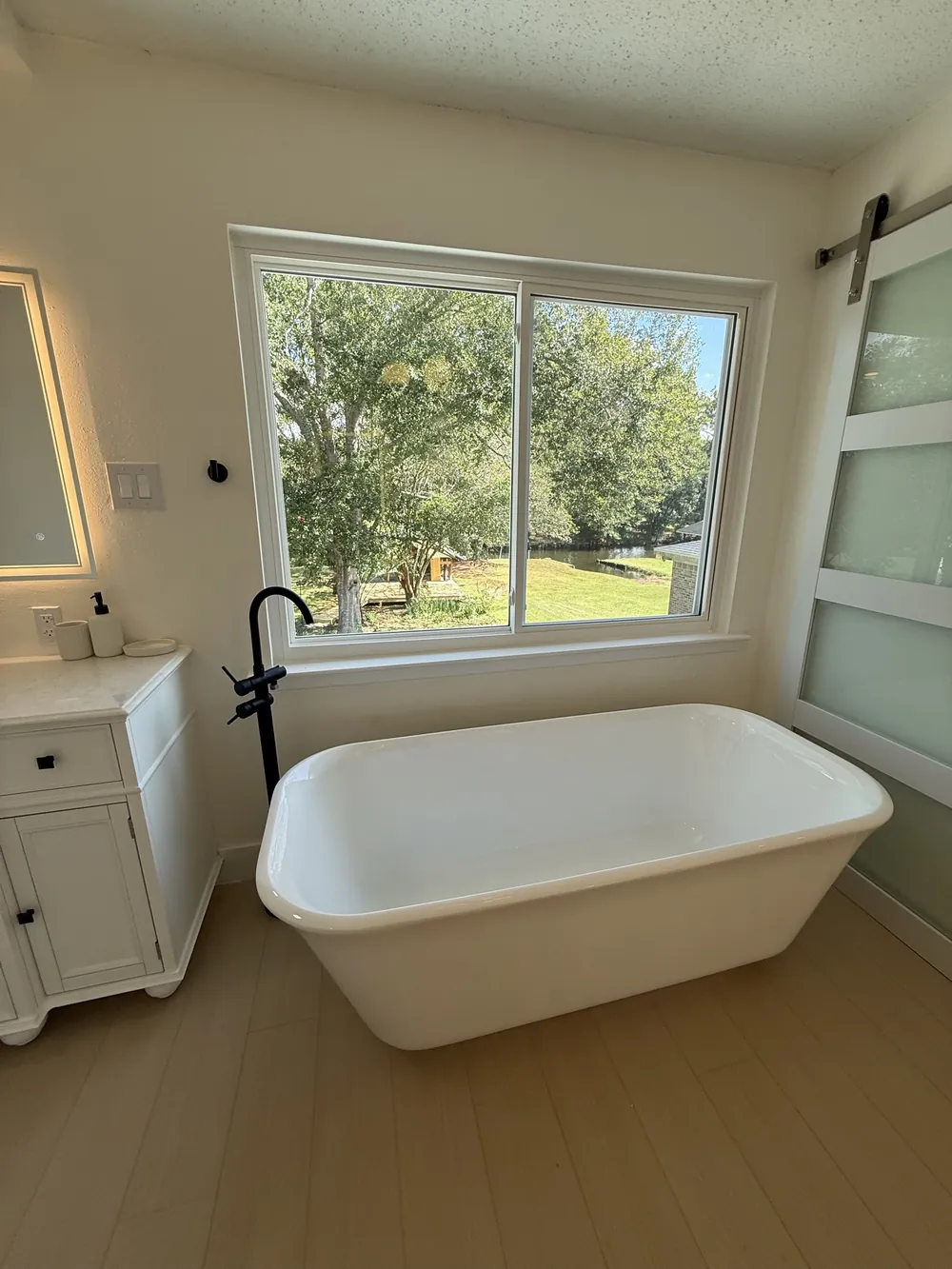 Primary bathroom with a freestanding soaking tub, matte black floor-mount filler, large window and a frosted glass barn door