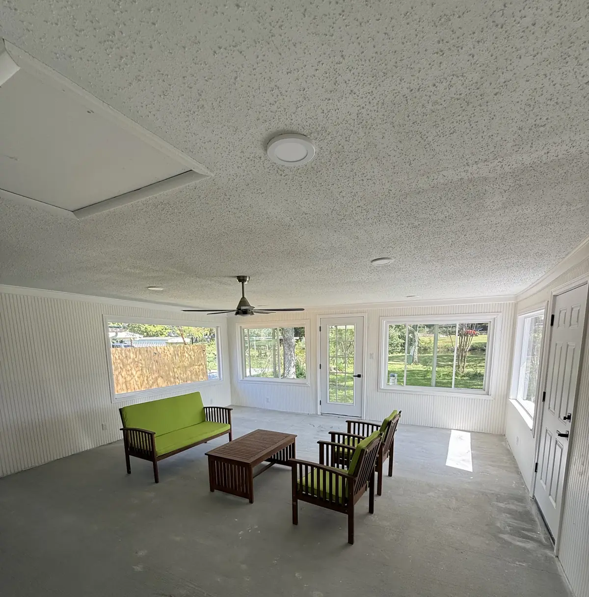 Bright enclosed sunroom with beadboard wainscot, a wall of windows, ceiling fan and finished concrete floor
