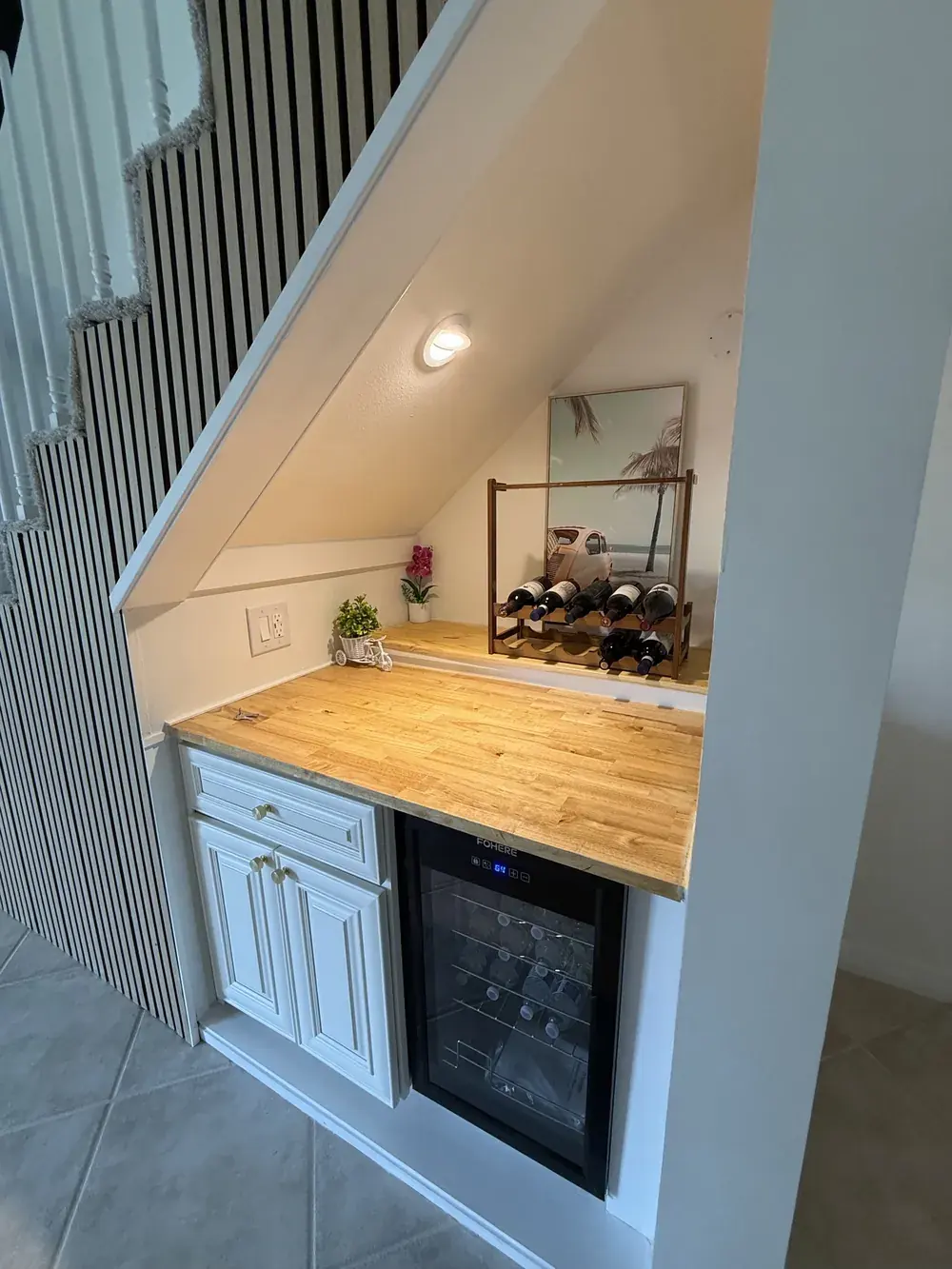 Wine bar built into the space beneath the staircase with butcher block counter, cabinet and a built-in wine fridge