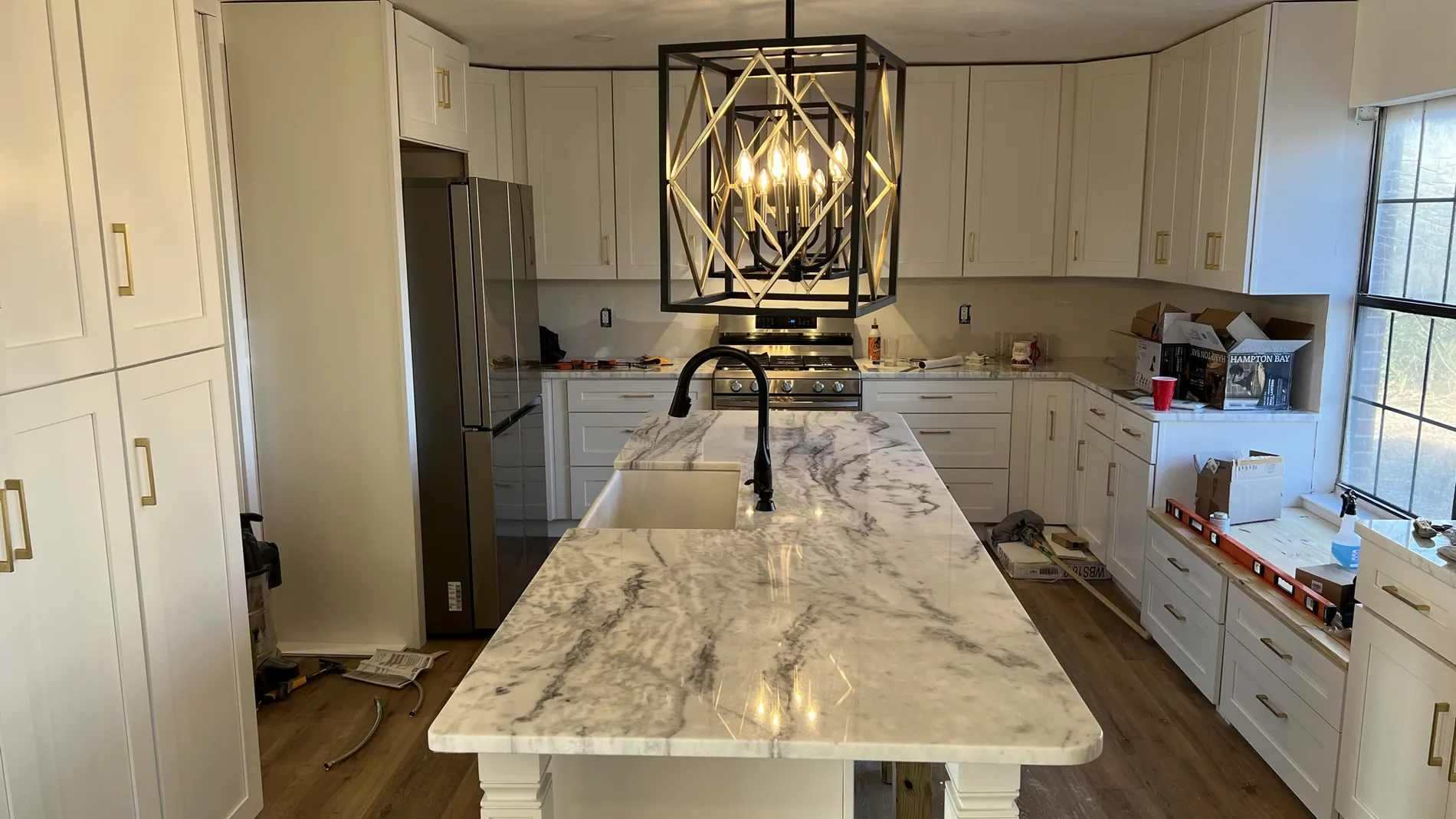 Kitchen with a large marble-topped island, farmhouse sink, white cabinetry, brass hardware and a black lantern pendant