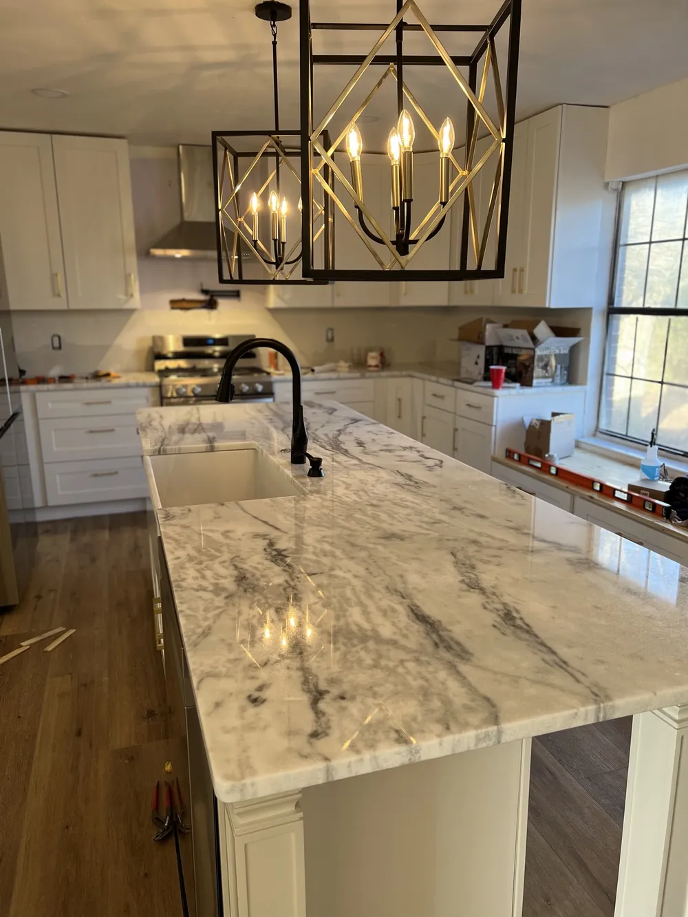 Large marble-topped island with a farmhouse sink, matte black faucet and a black and brass lantern pendant