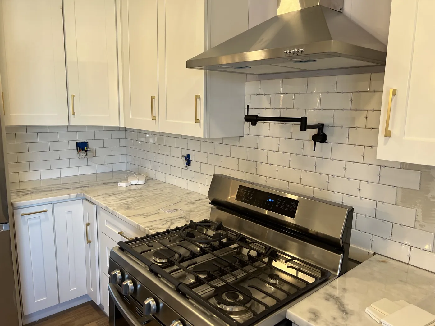 Kitchen range wall with a stainless gas range, chimney hood, matte black pot filler, white subway tile and marble counters