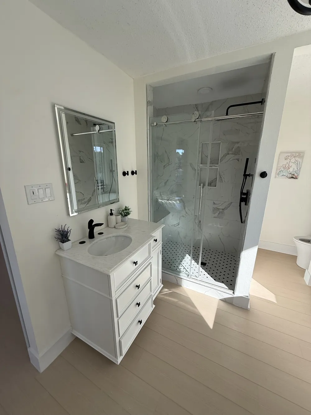 Bathroom vanity with quartz top, matte black faucet, backlit mirror and the tiled shower alongside