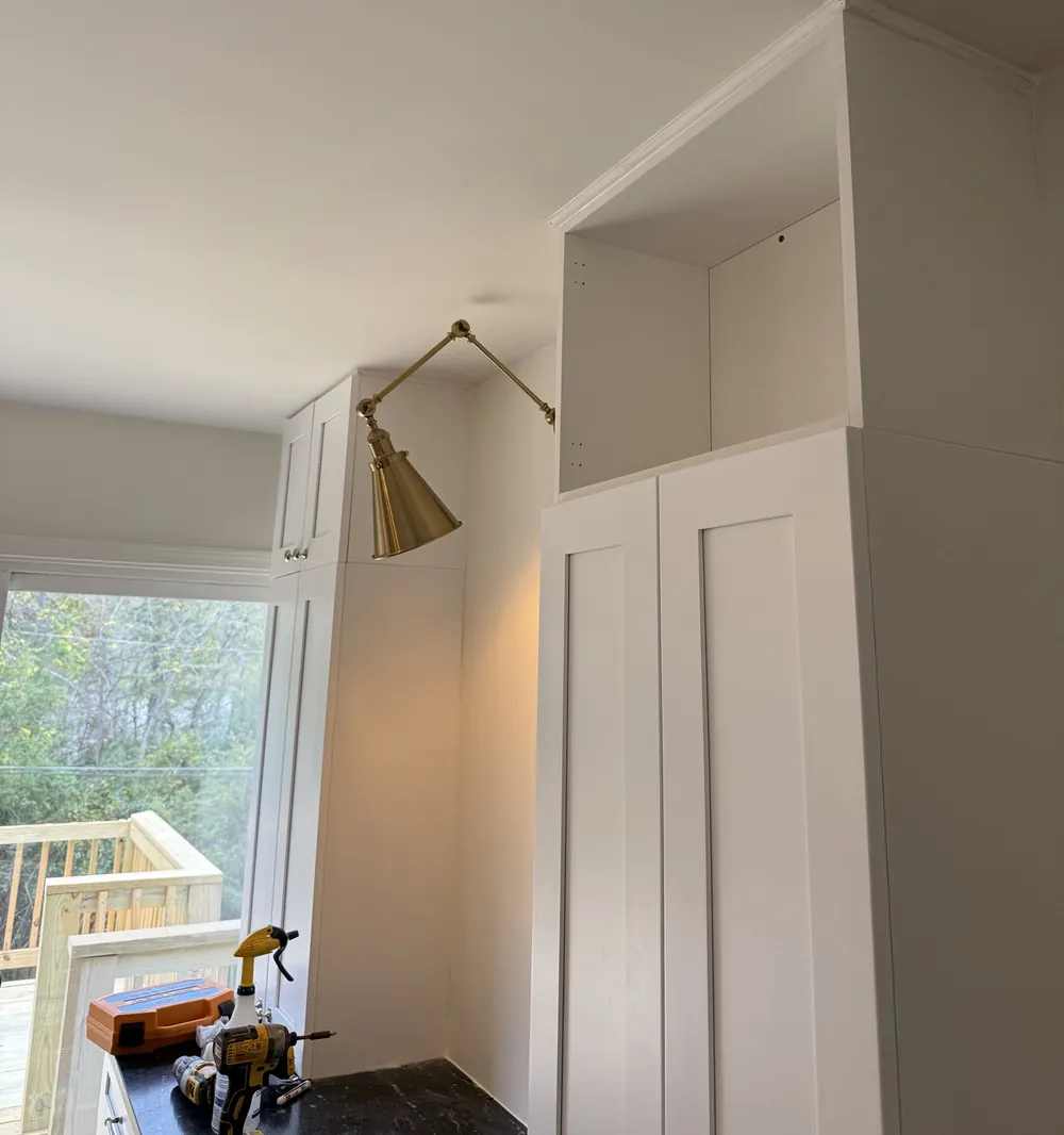 Floor-to-ceiling white pantry cabinets with stacked uppers, crown trim and an articulating brass wall sconce