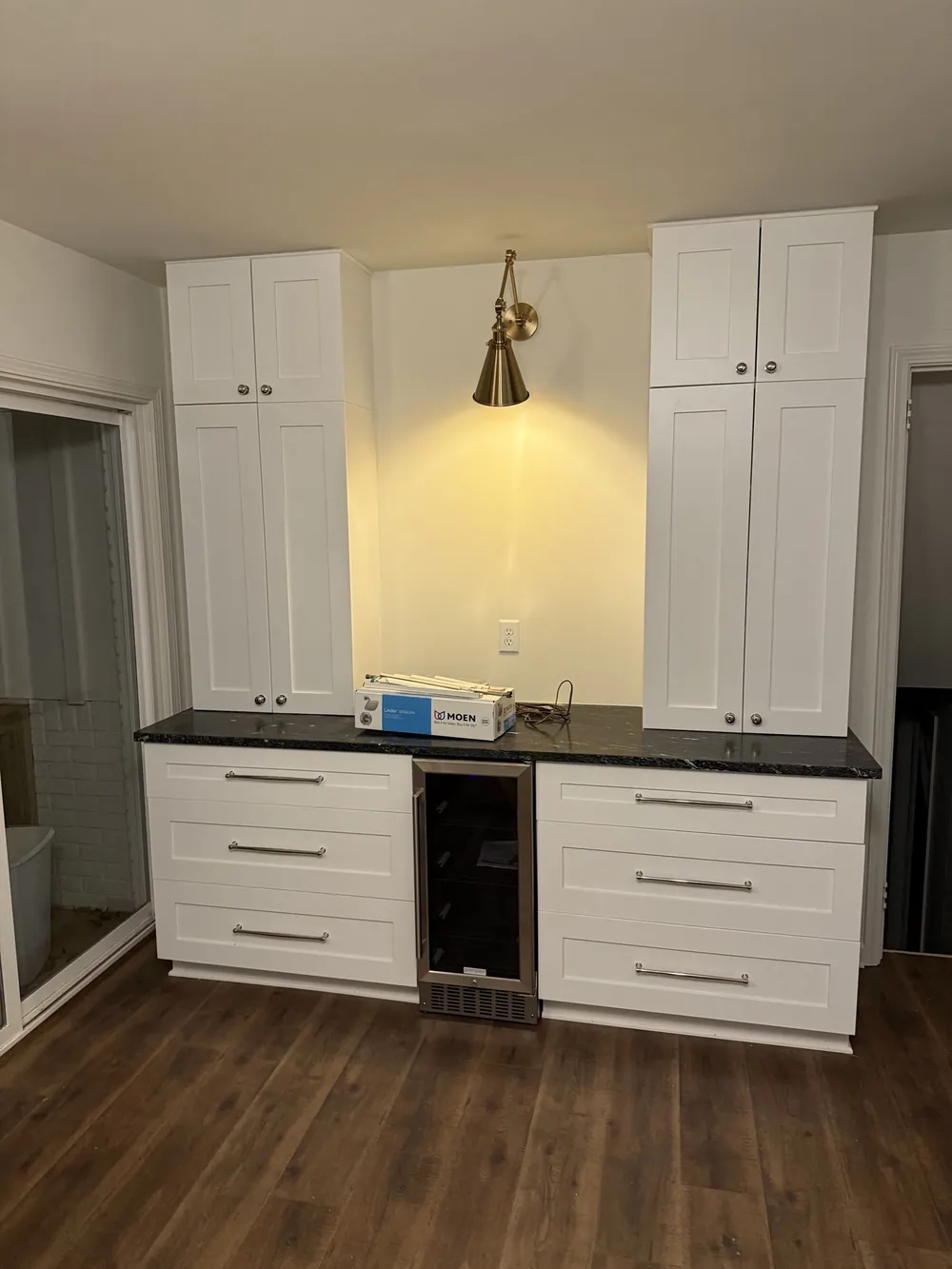 Coffee and beverage bar with white cabinets, black granite counter, undercounter wine fridge and a brass wall sconce