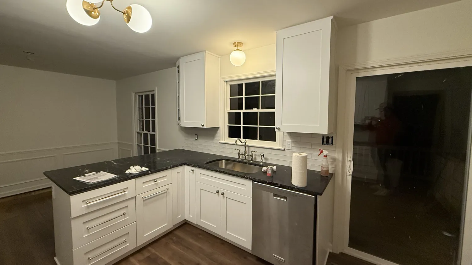 Finished kitchen with white shaker cabinets, black granite counters, white subway tile backsplash, brass lighting and wood-look plank flooring