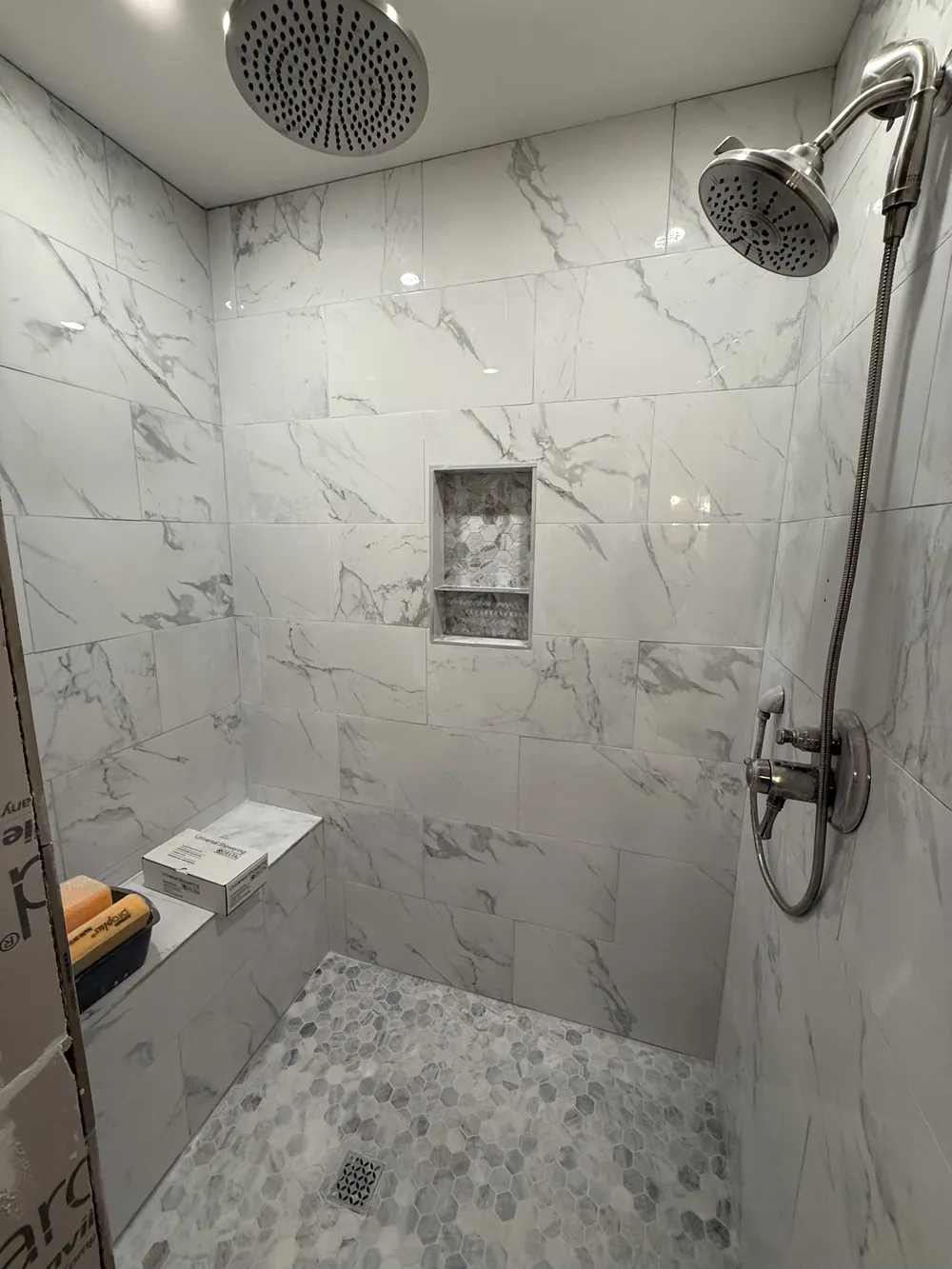 Tiled shower interior showing the overhead rain head, hand shower, recessed niche and hex mosaic pan