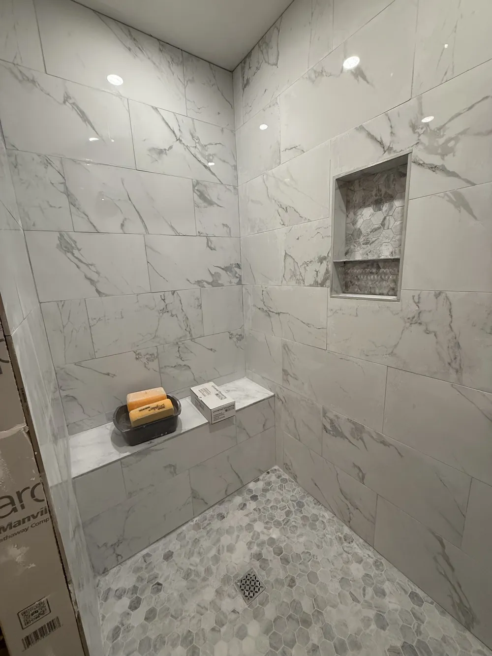 Walk-in shower tiled in large marble-look porcelain with a hex mosaic floor, recessed niche and a built-in bench